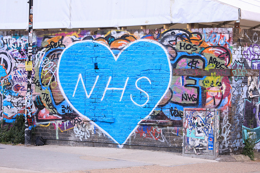 London, England - May 12, 2020. Coronavirus: Blue heart shape featuring NHS on a graffiti wall, Hackney, London.