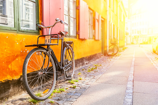 Brunette woman with white wireless headphones listening to music while walking with bicycle through the city