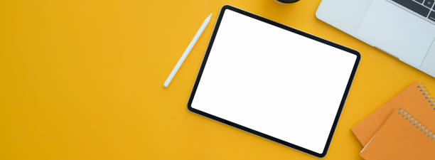 Top view of creative workspace with blank screen tablet, stylus, laptop and copy space on yellow desk