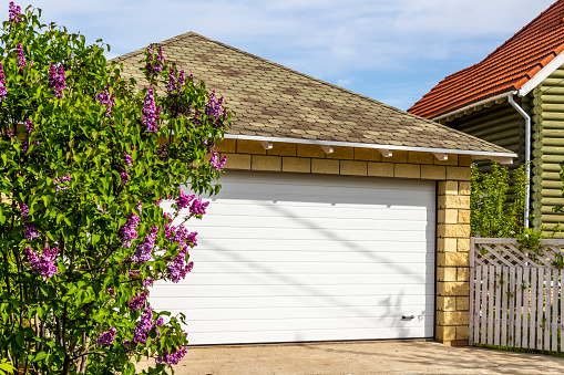 White garage doors of a private house and nearby lilac bushes.