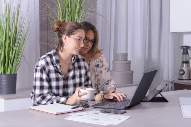 istock young woman working from home and drinking coffee and her mother behind watching her work. 1225722838