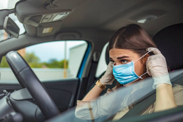 istock Young woman driving car with protective mask on her face. 1225724702