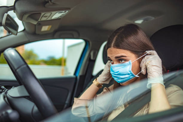 istock Young woman driving car with protective mask on her face. 1225724725