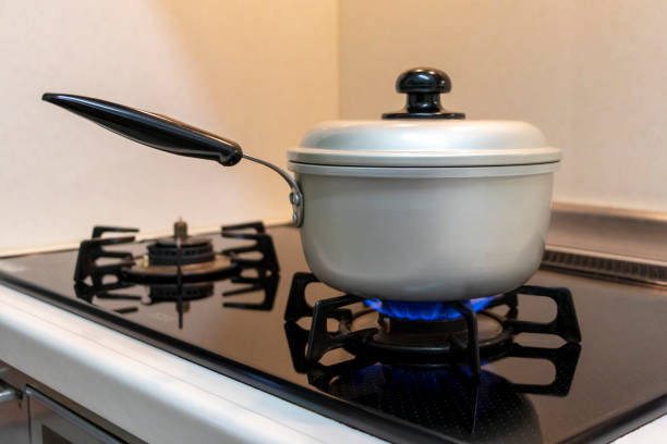kettle on stove with fire off, color photo. kitchen tile is pink and the stove is black. a beam of light passes through the glass of the stove