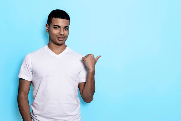 Young latin man isolated on blue background smiling and pointing aside, showing something at blank space.
