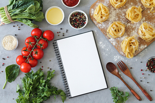 Healthy cooking concept. Recipe notebook and fresh spaghetti ingredients for making Italian pasta on stone background. Top view, flat lay and copy space