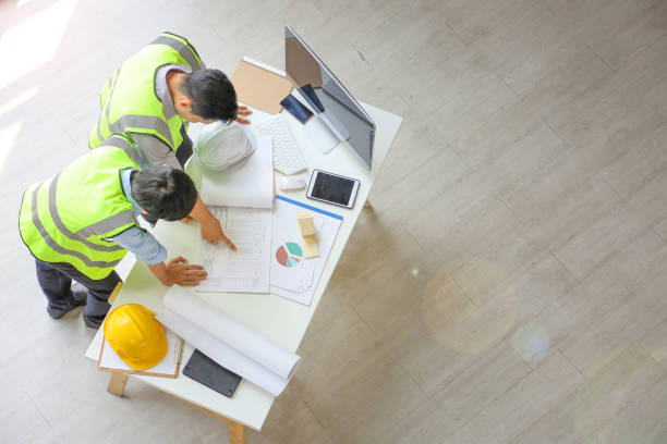istock Two Asian engineers wearing safety equipment while discussing over the future expanding business plan with blueprint of the factory inside the warehouse from the top view 1225736960