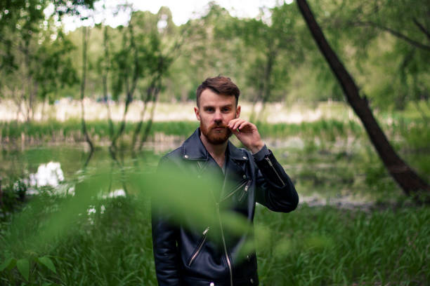 istock A young guy with a red mustache and a beard trembles with his mustache against a green forest looking to the right with foliage in the foreground 1225737728
