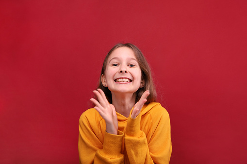 A happy girl in an orange retinue breaks in the palm of her hand and smiles. Red background.