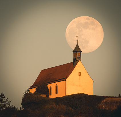 Church tower with cross in front of the super moon