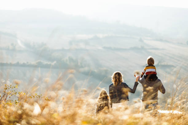 Rear view of a family standing on a hill in autumn day. Back view of a family standing on a hill in autumn day while father is aiming at distance. Copy space. eastern europe stock pictures, royalty-free photos & images