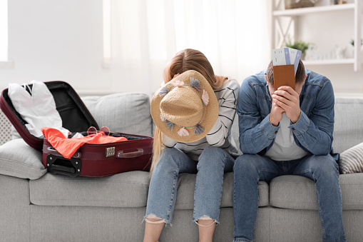 Ruined summer plans. Desperate couple suffering at home near packed suitcase for vacation, empty space