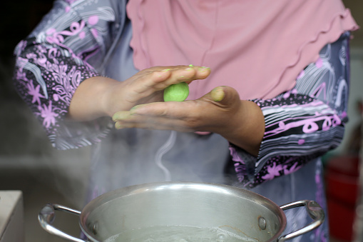A Muslim female adult is preparing 'onde-onde' (glutinuos rice balls with palm sugar filing coated with grated coconut) at home. She is home-based seller and preparing local delicacies during Ramadan month coincide with partial lockdown in Malaysia.
