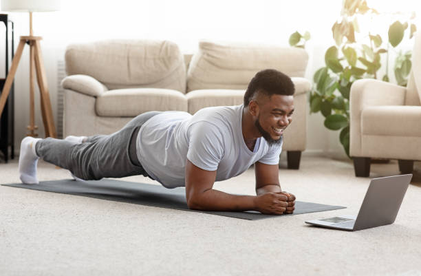 Sporty man training at home and watching online tutorial on laptop