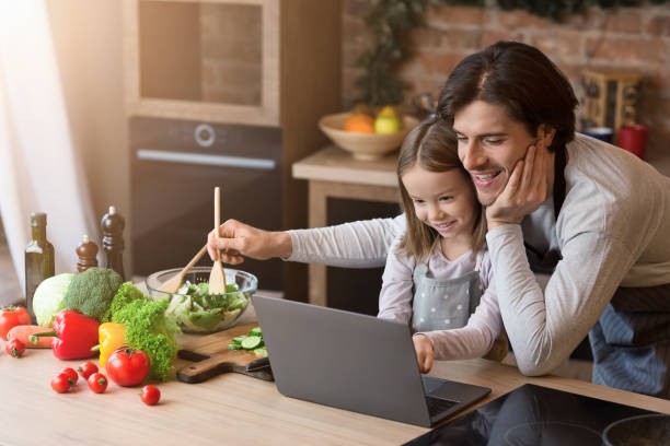 Dad and his little daughter using laptop, checking ingredients for dinner