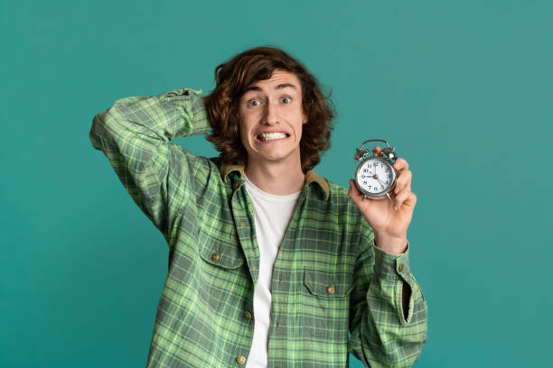 istock Time management. Millennial guy with alarm clock clutching his head in panic on turquoise background 1225748117