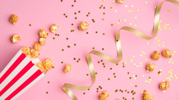 palomitas de maíz en cubo de papel rojo y blanco esparcidos sobre fondo rosa con cinta dorada y confeti. - star shape confetti red nobody fotografías e imágenes de stock