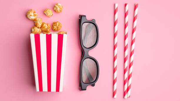 istock Flat lay composition with popcorn in striped cardboard box, 3d glasses and drink straws on pink background. Watching movie at cinema concept. 1225749076