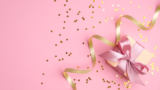 Caja de regalo de moda con lazo de cinta rosa, serpentina dorada y estrella de confeti en la vista superior de fondo rosa. Plano lacomposición para cumpleaños, Navidad o boda. photo