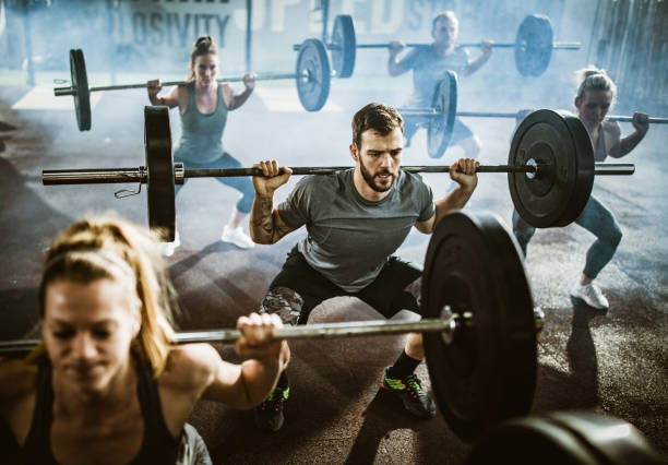 ジムでのクロストレーニングでバーベルで強さを行使するアスリートのグループ。 - weight training crouching barbell weightlifting ストックフォトと画像