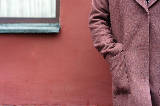 Portrait of a woman hand  in the pocket in a burgundy coat view from the back against a red wall. The concept of minimalism in composition, without a face. Impersonal. Winter snowflake