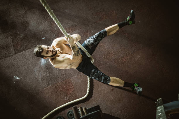 sopra la vista dell'uomo atletico che sale la corda in palestra. - climbing clambering hanging rope foto e immagini stock