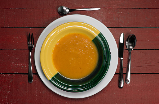 plate of pumpkin soup on a red wooden table
