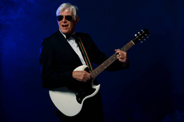 istock Musician Guitarist Active senior Handsome man playing guitar. Blue  background, with rays of light and special effects smoke. 1225756505