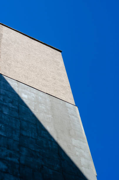 Concrete wall against the blue sky. The play of light and shadow on the facade of a tall building. Minimalism in modern architecture. Selective focus.