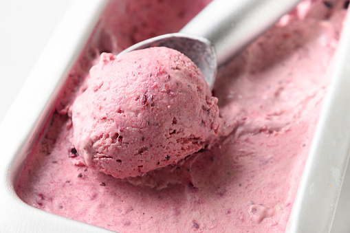 Homemade berry ice cream in metallic tub with scoop on white background. Close up.