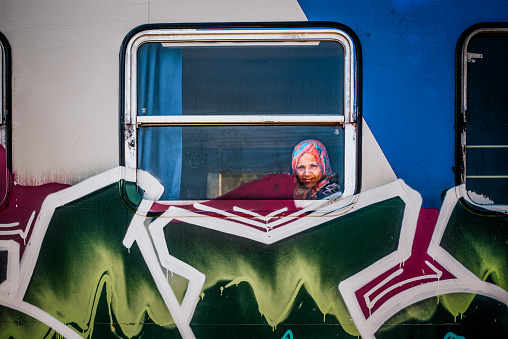 Woman looks out of the window of a graffiti trian traveling along the coast of Sicily towards Noto