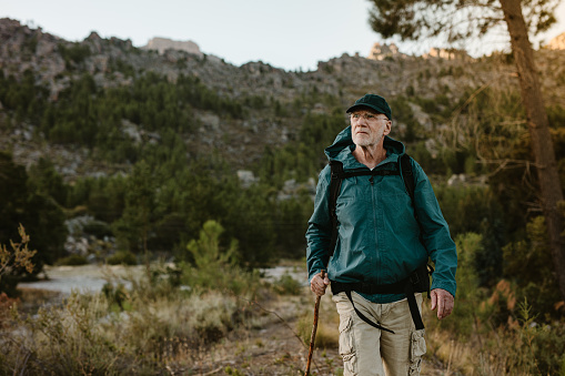 Senior man walking on mountain trail. Confident mature man carrying a backpack hiking in nature.