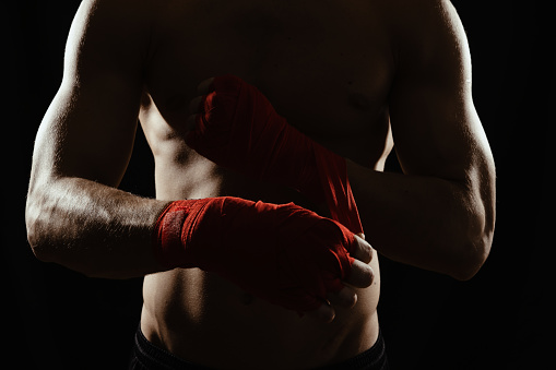 Close-up of the hands of a young boxer who winds red bandages before a match, fight or training.