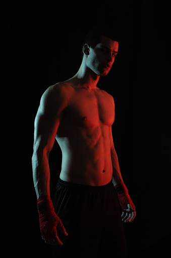 Portrait of male boxer posing in boxing stance against black background in red and white light