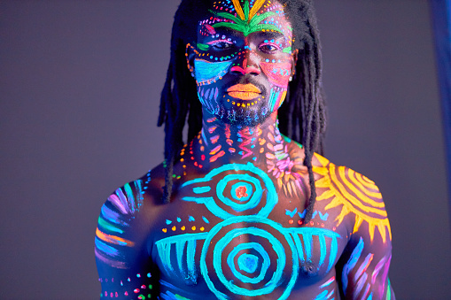 portrait of young black man with colorful ethnic fluorescent prints on his muscular body, shirtless guy posing at camera, colorful makeup and body art