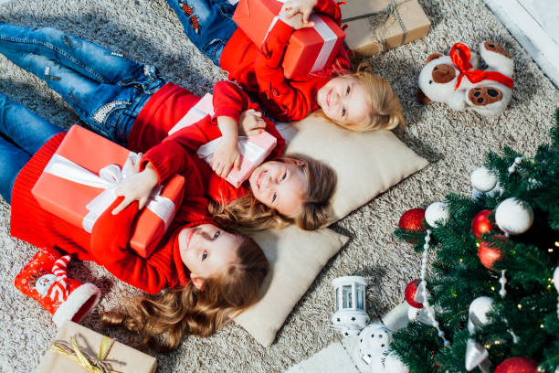 três meninas estão perto de uma árvore de natal com presentes feriado de ano novo - clock baby christmas small - fotografias e filmes do acervo