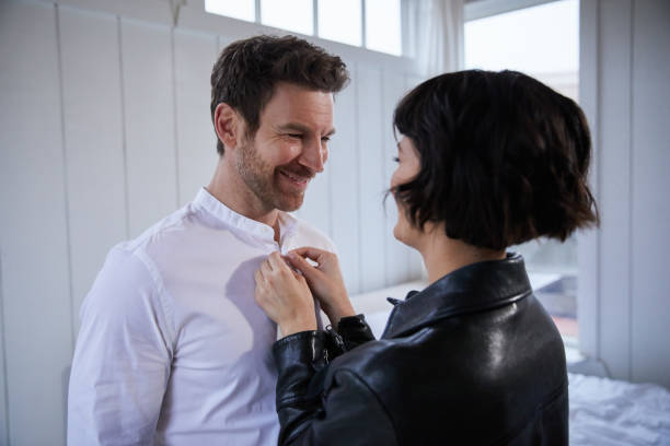 istock Smiling young woman buttoning her husband's shirt while getting dressed 1225774625