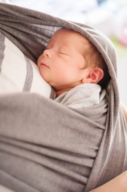 The baby is always close to her mother Close-up shot of a mother carrying a sleeping baby in a sling baby carrier stock pictures, royalty-free photos & images