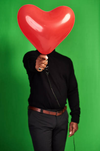 Cropped shot of a man posing with a heart-shaped balloon in front of his face
