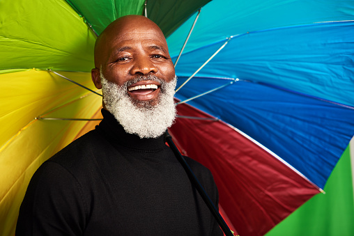 Shot of a senior man posing with a colorful umbrella over his head
