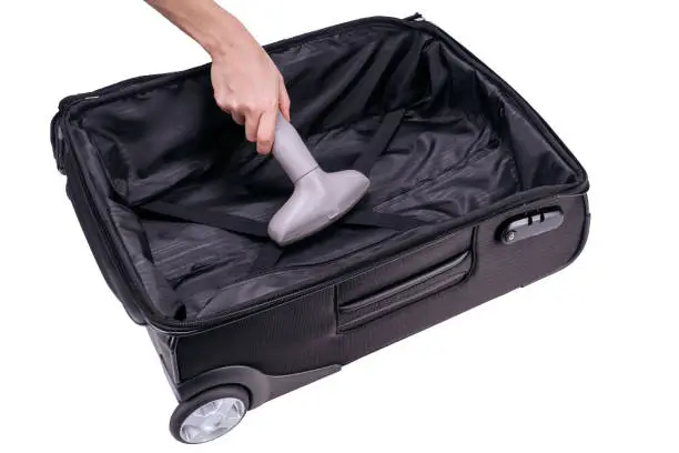 Hand vacuum-cleans black suitcase with the gray vacuum-cleaner.