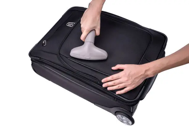 Hand vacuum-cleans black suitcase with the gray vacuum-cleaner.