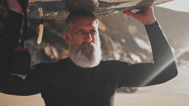 Close up senior handsome man carrying surfboard at the beach