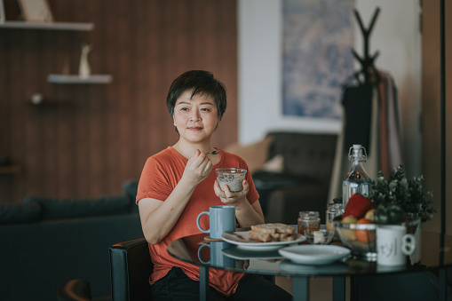 a mid adult woman enjoying her breakfast in the morning at her apartment looking away smiling