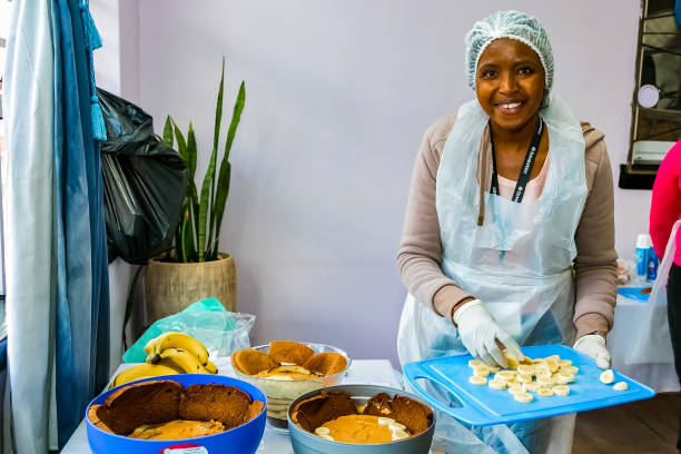 i volontari della comunità soup kitchen preparano i pasti per i bambini africani nell'orfanotrofio - homelessness food in a row people foto e immagini stock