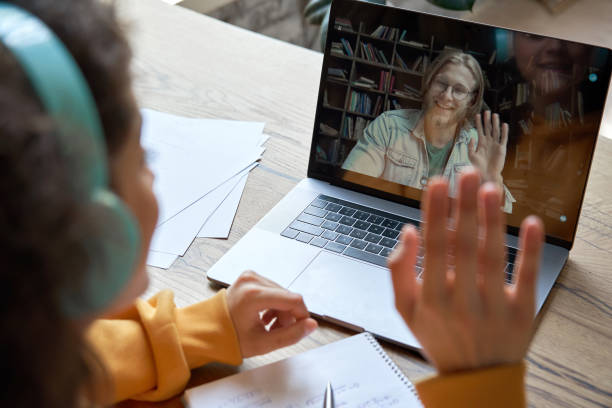 Hispanic teen girl school college student distance learning waving hand studying with online teacher on laptop screen. Elearning zoom video call, videoconference class with tutor. Over shoulder view. Hispanic teen girl school college student distance learning waving hand studying with online teacher on laptop screen. Elearning zoom video call, videoconference class with tutor. Over shoulder view. zoom classroom stock pictures, royalty-free photos & images