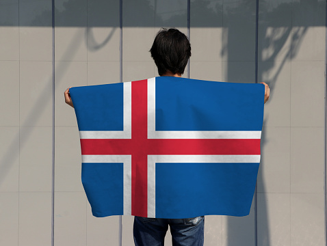 The man is holding Iceland flag on his shoulder and turn back on grey background.