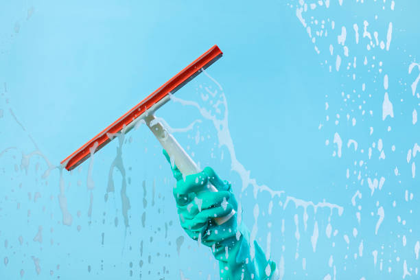 Dishwashing gloves and cleaning wiper isolated on blue soapy glass. Squeegee wipe the glass with soap foam
