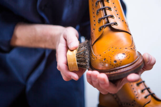 ideias de calçados. close-up de limpeza mãos masculinas com escova de limpeza para botas de derby bronzeado. trabalhando em blue apron. orientação horizontal da imagem - bristle brush part - fotografias e filmes do acervo