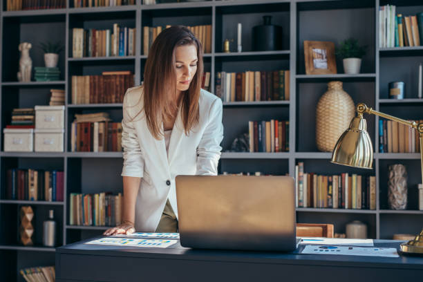 Woman stands at desk and looks at documents.